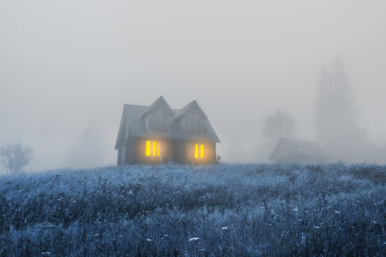 Old wooden house.Light from window of an old cabin. Spooky misty foggy forest. Halloween holiday celebration background