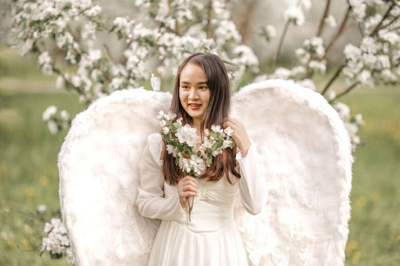 A beautiful woman angel stands in a blooming apple orchard.