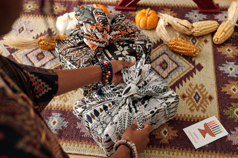 Above angle of young African American woman tying knot on top of packed and wrapped giftbox on table with ears of corn