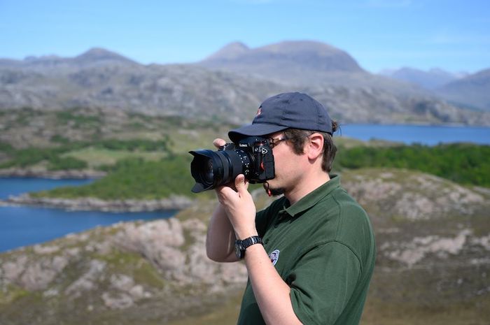 young man taking a photo with a reflex type camera, with hills and lakes in the background