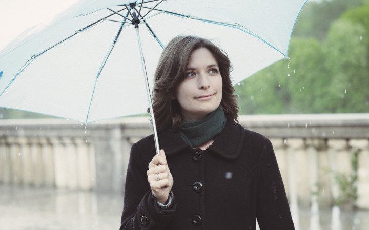 Young woman holding a blue umbrella under the rain.