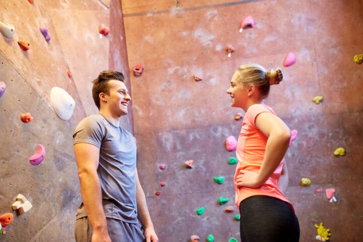 young man and woman with sports clothing, smiling at each other in front of a climbing wall