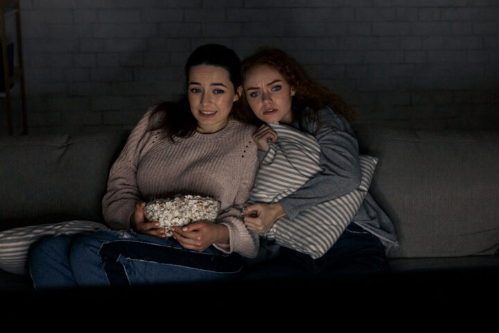 Two young girls scared while watching a horror film on TV