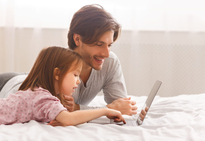 dad and his daughter using a laptop on the bed