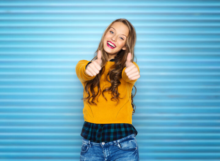 people, gesture and fashion concept - happy young woman or teen girl in casual clothes showing thumbs up over blue ribbed wall background