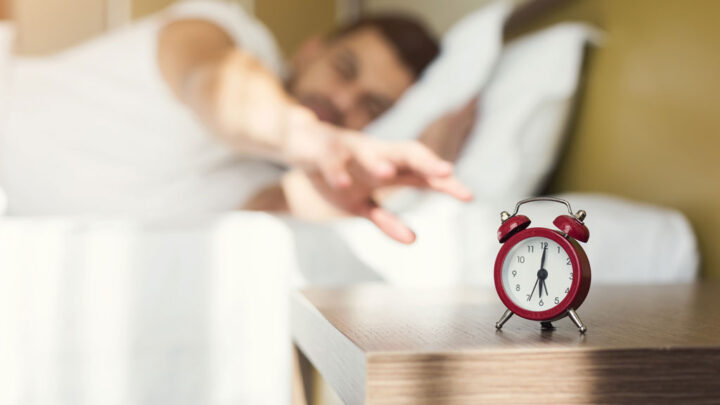 man in bed turning off alarm clock