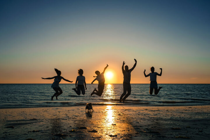 silhouette of people jumping in front of sunset on the beach