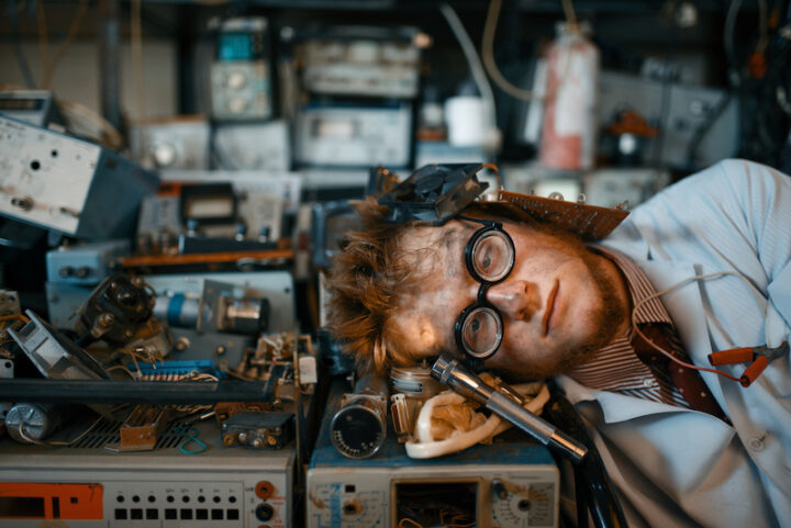Strange engineer sleeping on devices in laboratory. Electrical testing tools on background