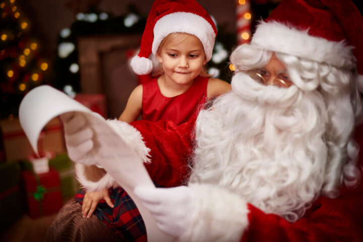 young girl sitting next to Santa Claus who is reading her wish list