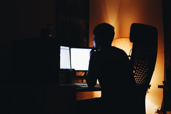 man sitting at his desk in front of his computer in the dark