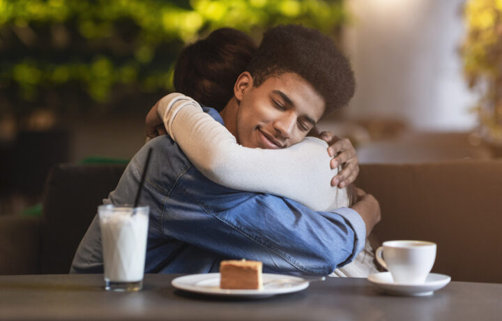 Peaceful beloved mixed race couple hugging with affection at cafe, copy space