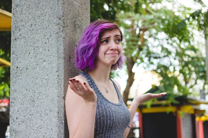 young woman with purple hair raising her eyebrows and shrugging her shoulders