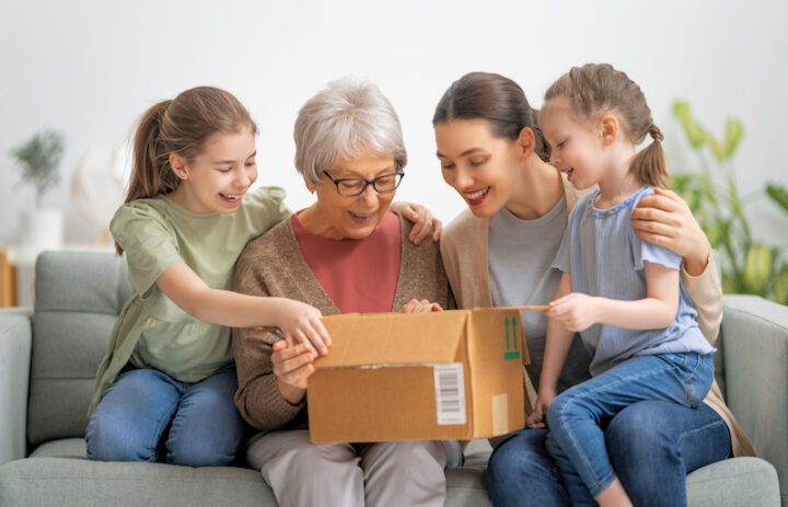 Grandmother, her daughter and granddaughters are unpacking cardboard box at home.