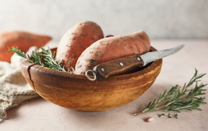 Sweet potatoes in a large wooden bowl with rosemary, close up.