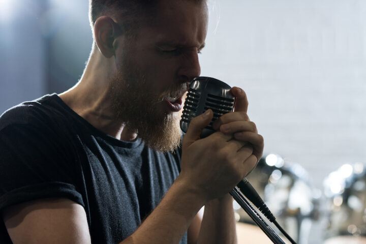 Side view portrait of handsome bearded man singing to microphone during band performance on stage, copy space