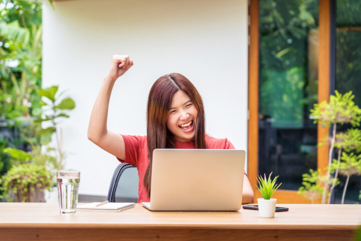Asian business woman using technology laptop and celebrating when job success form working from home in outdoor home and garden, startups and business owner, social distancing and self responsibility