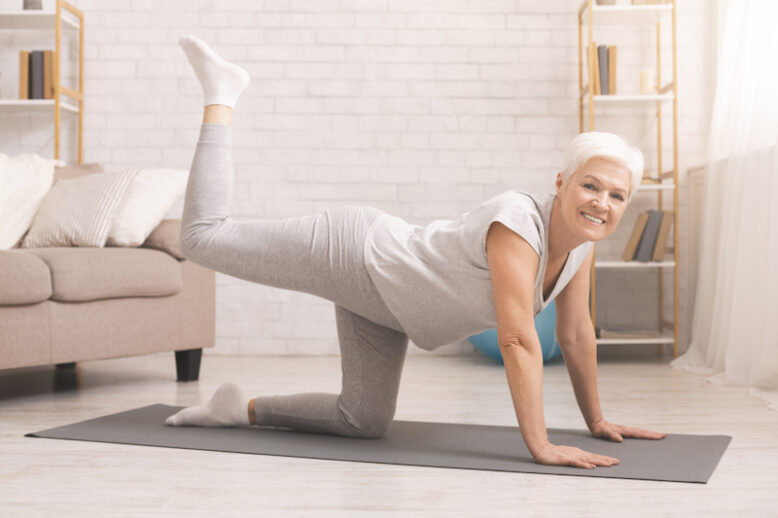 Senior fitness lady standing on all fours, straightening leg up, exercising at home