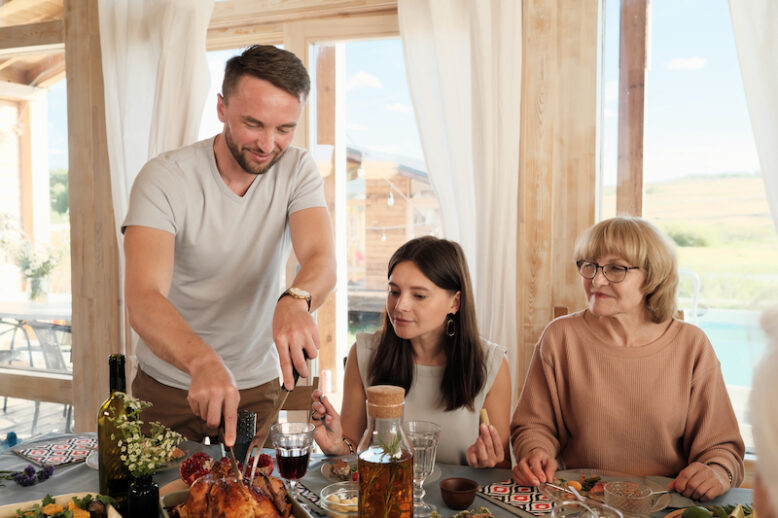 Man cutting fried turkey while sitting at the table with his family they celebrating Thanksgiving Day at home