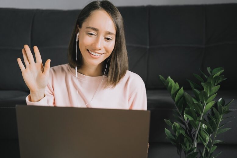 Happy young woman using laptop, calling her friends or family by video chat with headphones and waving her hand