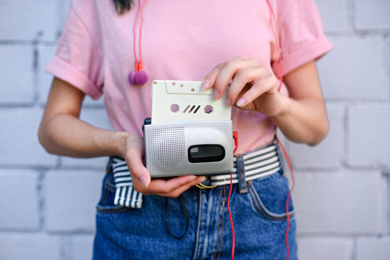 cropped shot of woman with earphones holding retro cassette player and audio cassette in hands