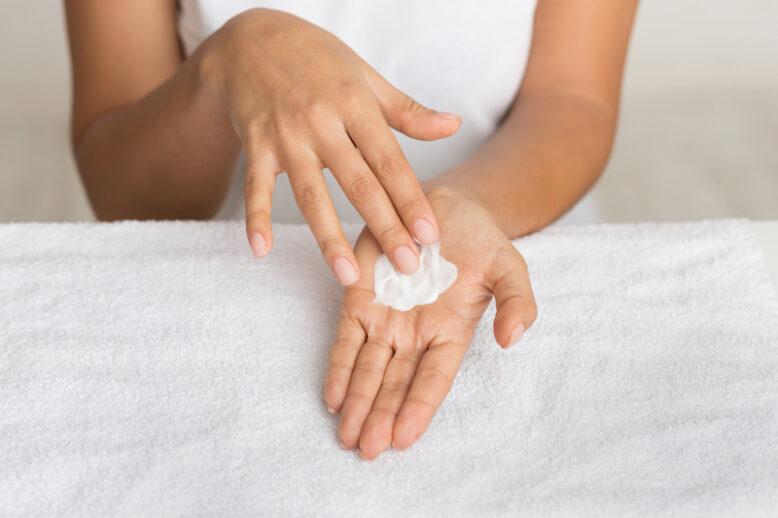 Skin nutrition. Girl spreading nourishing cream on palm against towel