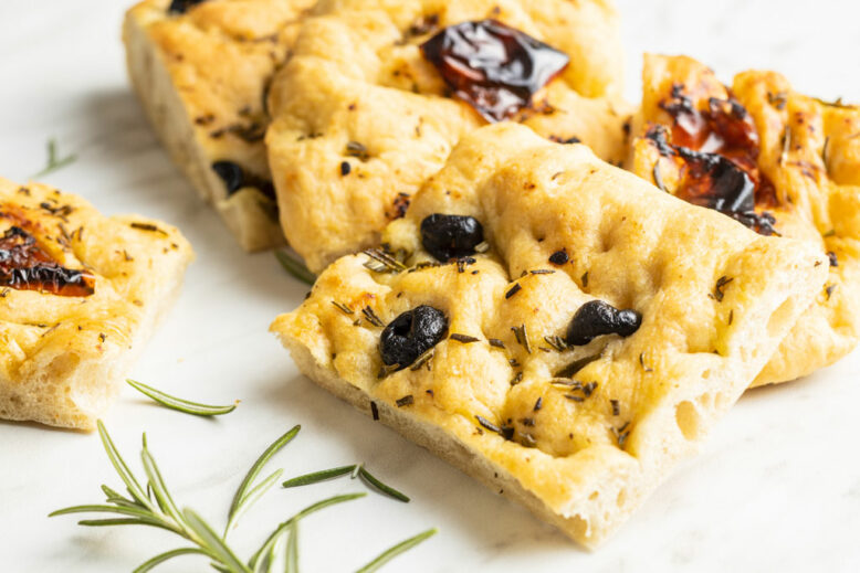 Homemade Italian Focaccia with dried tomatoes and olives on kitchen table.