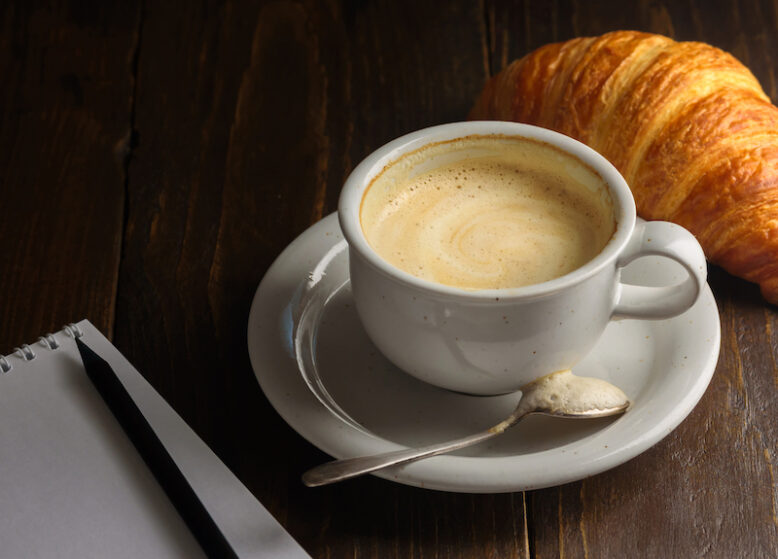 Cappuccino with croissant on dark wooden background. Text space. Blank notepad and pencil near it