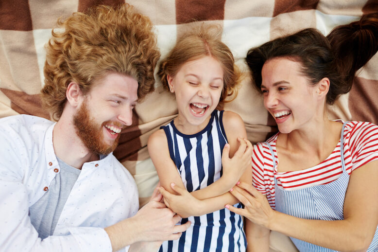Playful parents tickling their daughter and laughing altogether