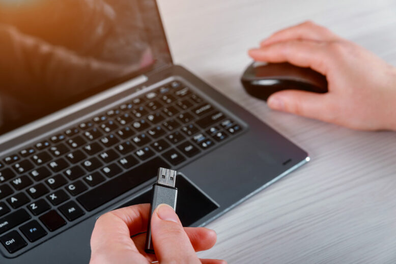 Hand of a woman holding a USB flash stick device connected to Laptop computer on white table