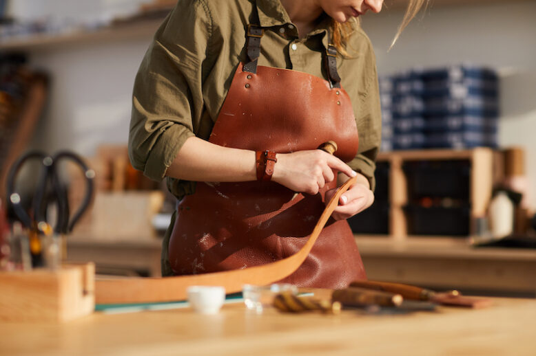 Mid section portrait of female craftsman working with leather in tannery shop