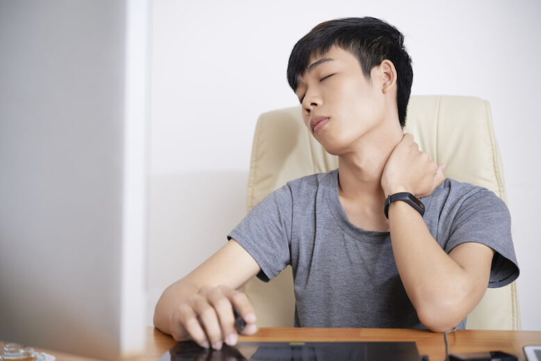Young man suffering from pain in his neck after long day of work