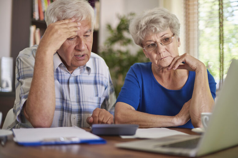 an elderly couple trying to find a solution, sitting on a desk with laptop and documents