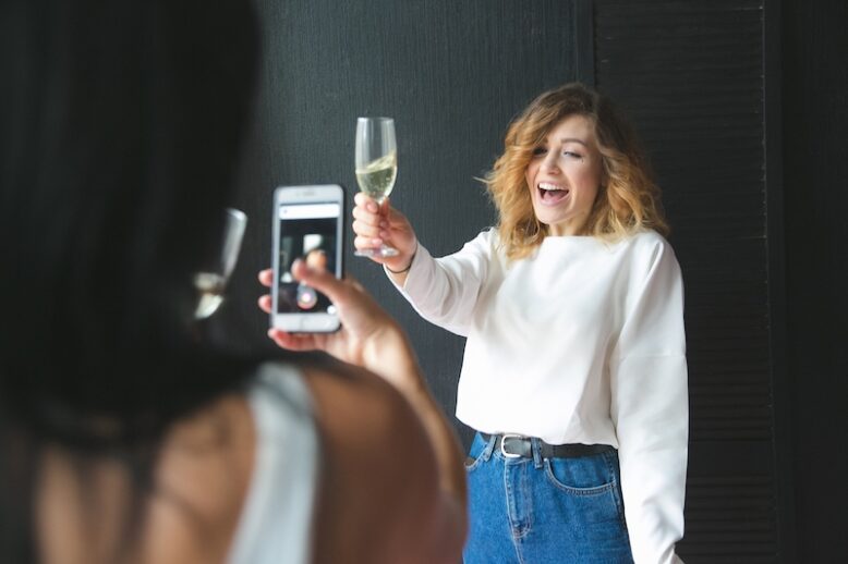 girl holding up champagne glass and being photographed with a phone