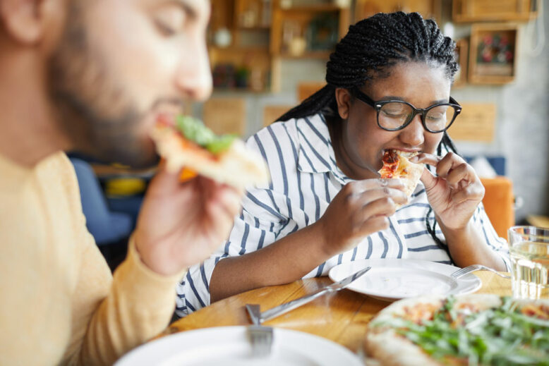 Two young hungry persons eating appetizing italian pizza in cafe during lunch break