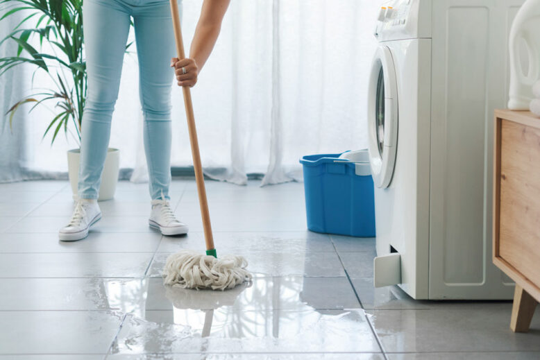 Broken washing machine leaking on the floor, a woman is cleaning with a mop