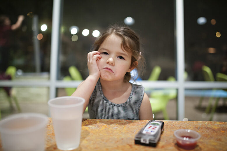 young girl sitting at a dining table with a sulky expression