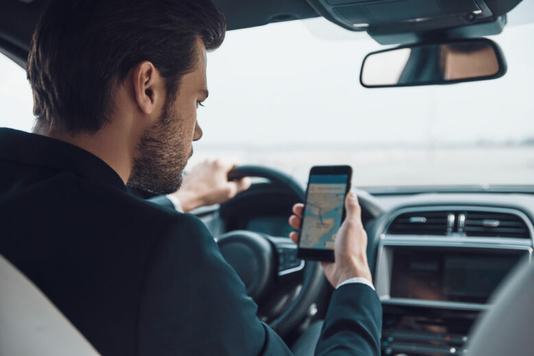 Rear view of young man in full suit using smart phone to check the map while driving a car