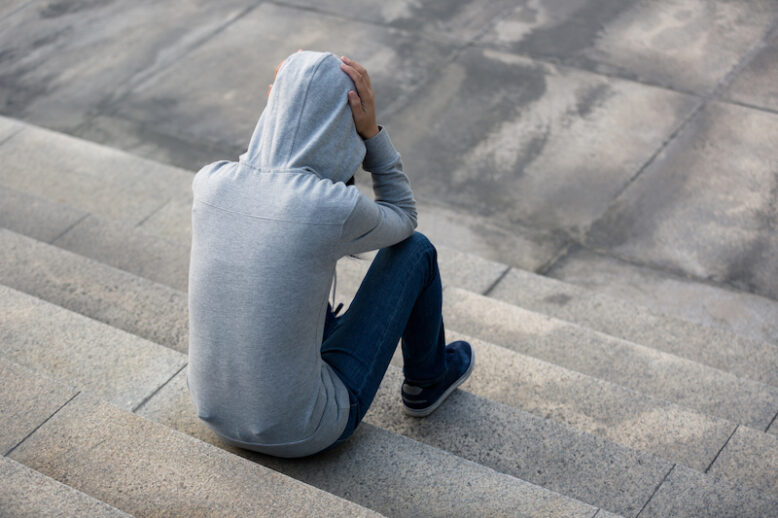 person with hooded shirt, sitting alone in city stairs with hands on the head