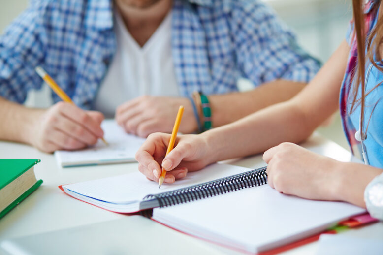 Hand of student with pencil carrying out written task or writing lecture