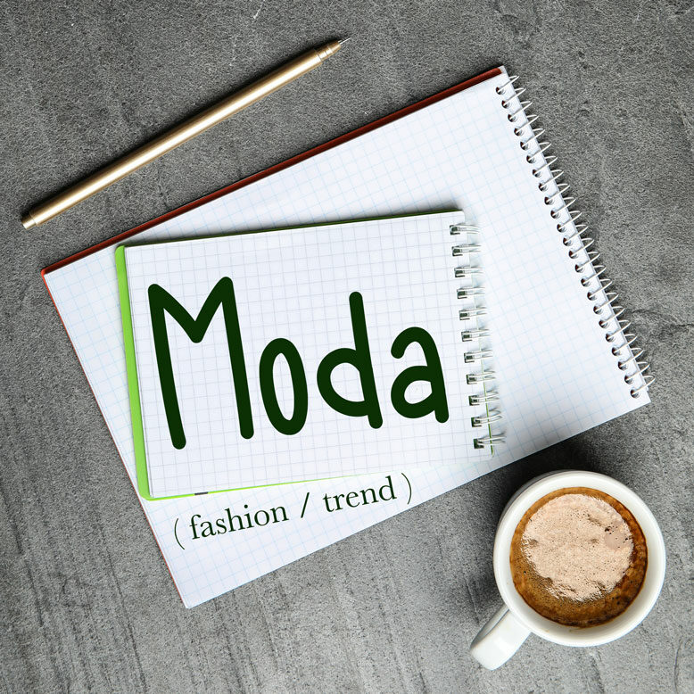cover image with the word “moda” and its translation written on a notepad next to a cup of coffee