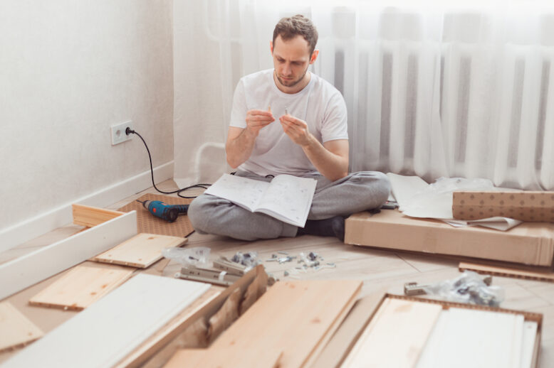 Man self-assemblies wooden furniture at home without master.