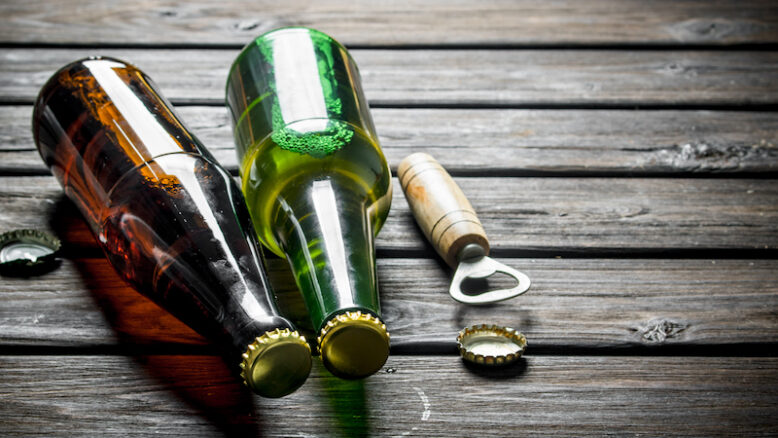 Beer in glass bottles and opener. On wooden background