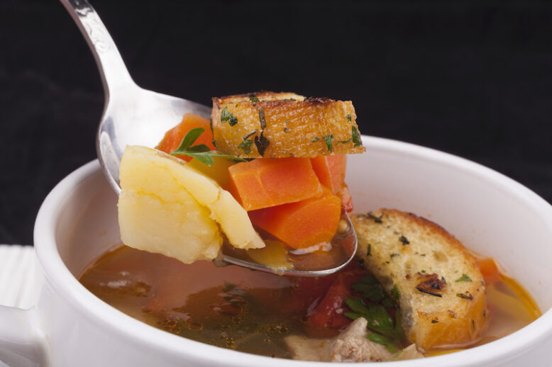 Vegetable soup on a spoon with bread close-up  on dark backgroun