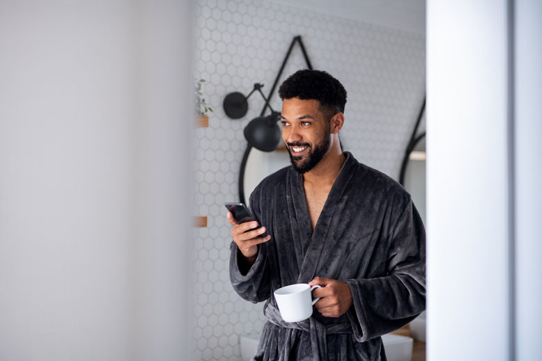 A young man with coffee and bathrobe indoors in bathroom at home