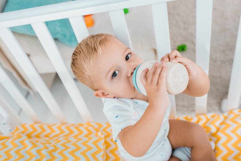 adorable toddler drinking out of baby bottle in crib