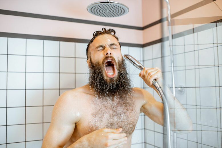 Homme barbu se sentant choqué en prenant une douche avec de l'eau froide dans la salle de bain à la maison