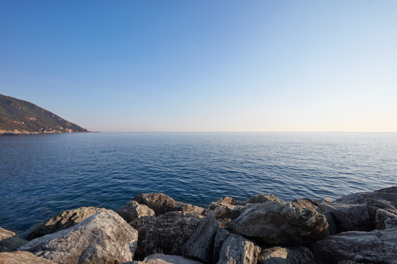 Mediterranean blue, calm sea with rocks and coast, clear sky in Italy