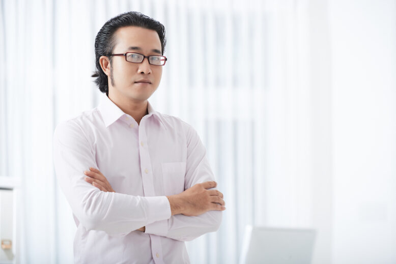 Homme asiatique sérieux adulte à lunettes et tenue formelle tenant les mains croisées en regardant la caméra