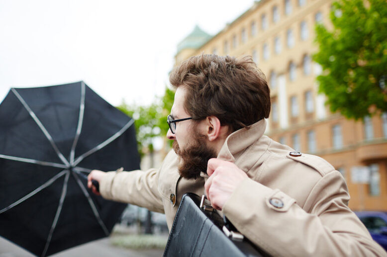 Businessman with umbrella confronting wind while going to work