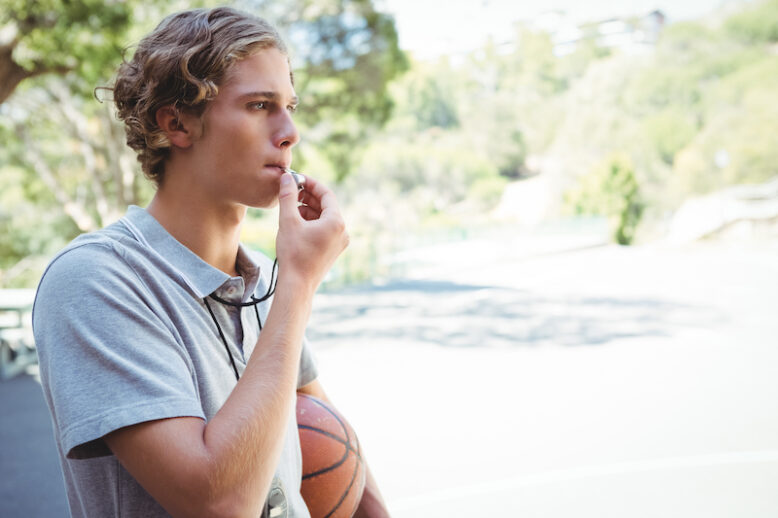 Man with basketball whistling while standing in basketball court